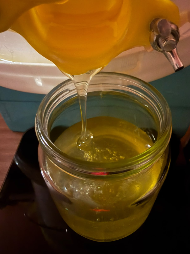 Golden honey being poured into a glass jar